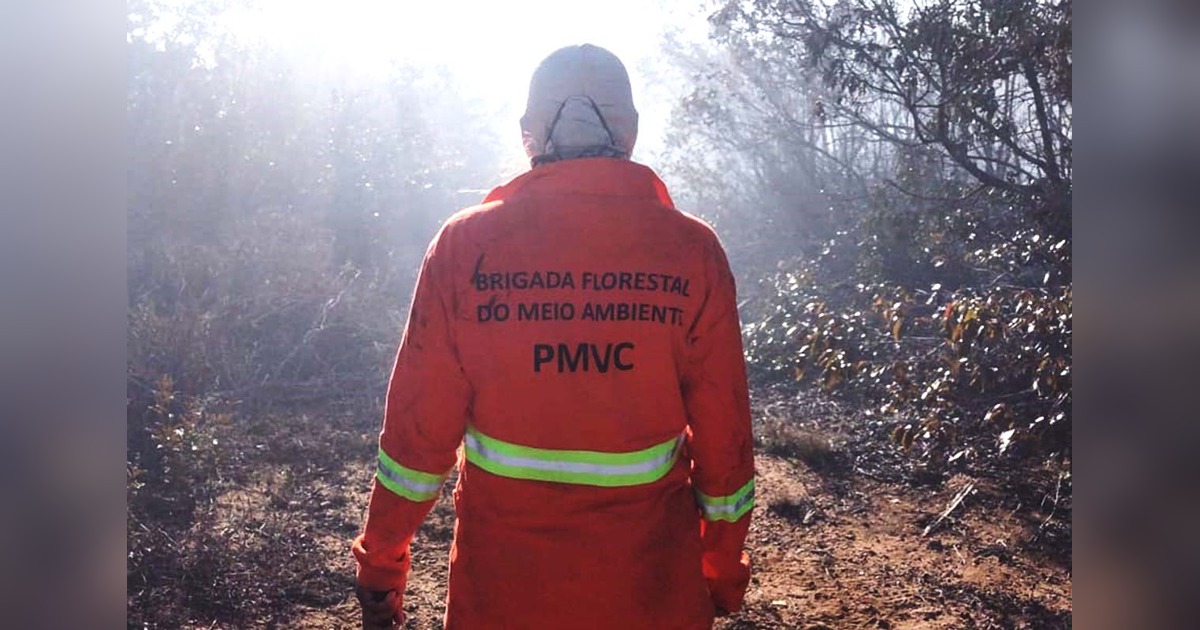 Brigadista de costas, com uniforme laranja identificado como Brigada Florestal do Meio Ambiente da PMVC, em área de vegetação