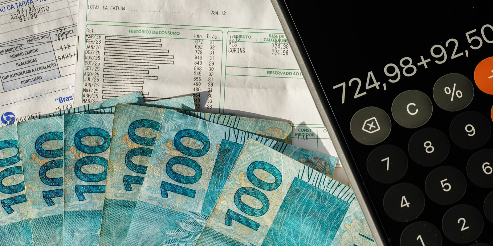 Notas de cem reais ao lado de calculadora e documentos