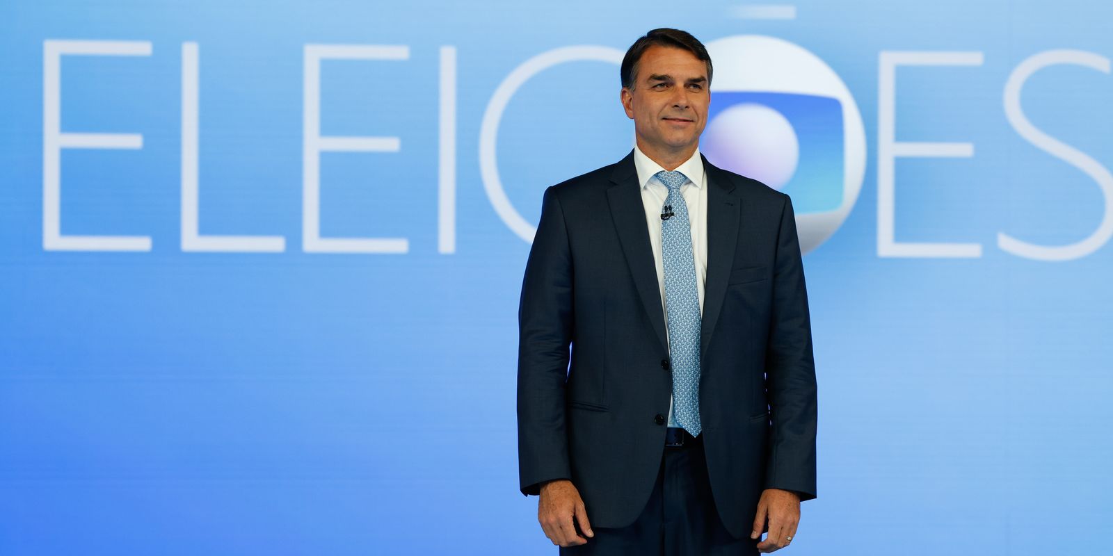 Flávio Bolsonaro diante do cenário azul do debate da TV Globo.