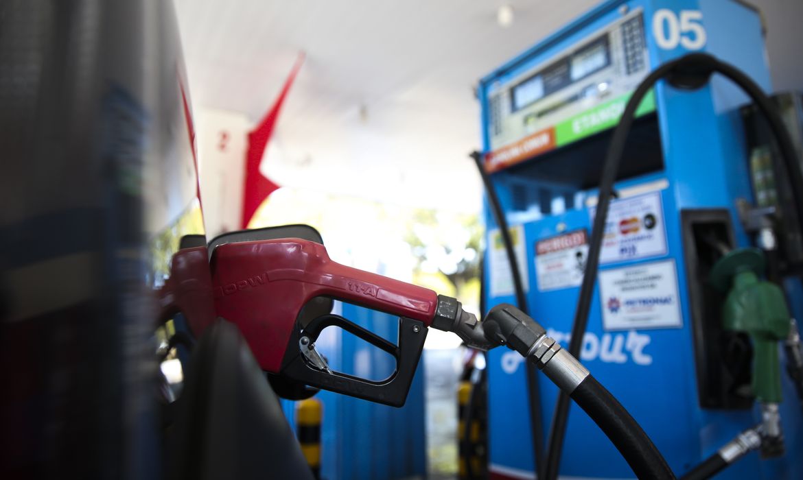 Bico vermelho abastecendo veículo, com bomba azul de combustível ao fundo