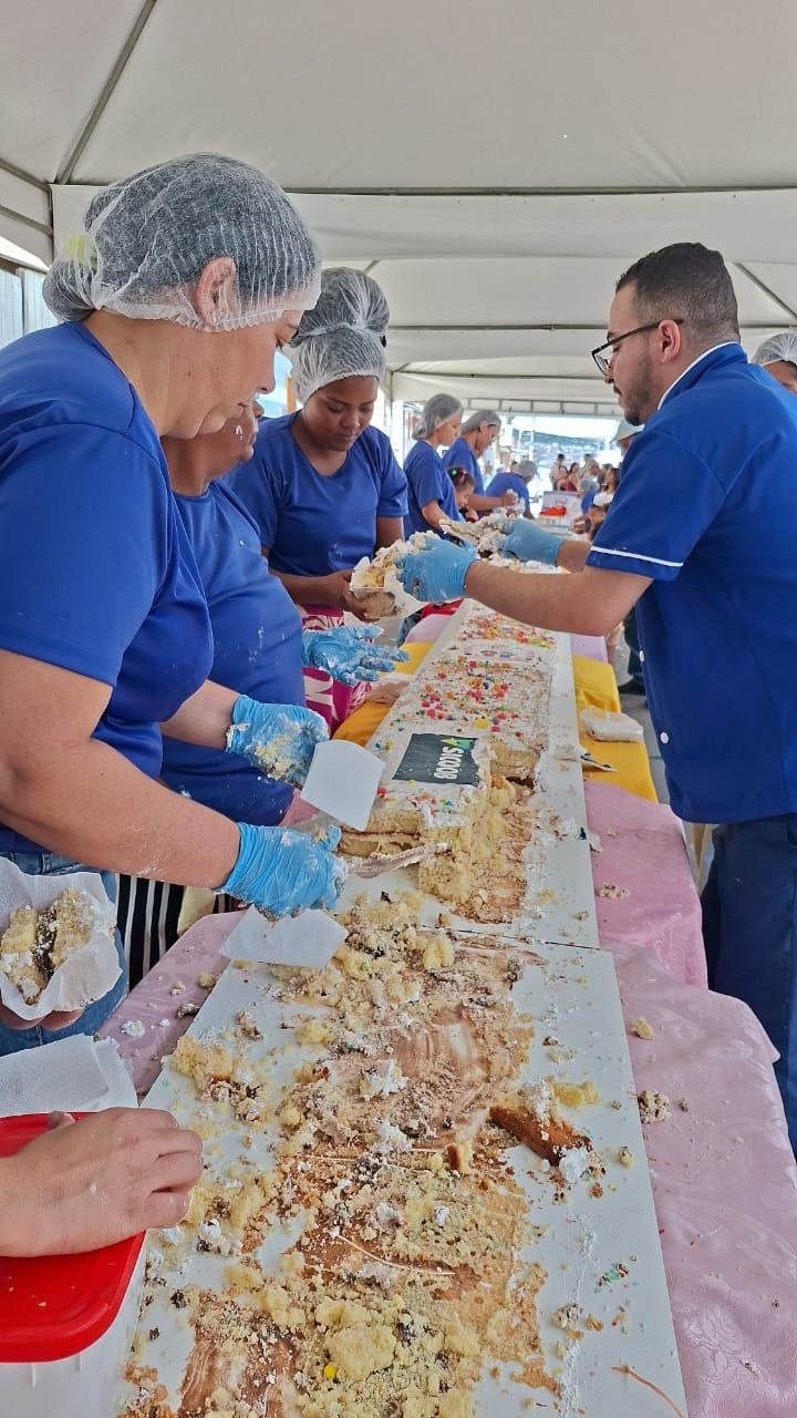 Participantes cortam e servem porções do bolo durante a ação Gigante Solidário