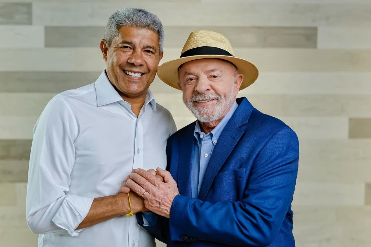 Jerônimo Rodrigues e Lula sorrindo e segurando as mãos; Lula usa paletó azul e chapéu de palha