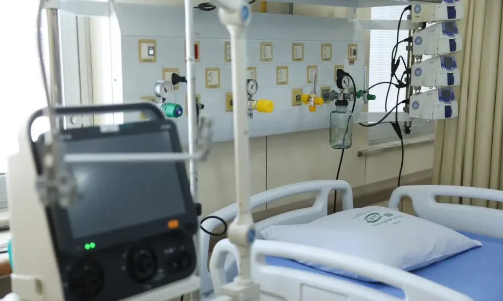 Leito hospitalar com travesseiro, monitor e equipamentos médicos ao lado da cama