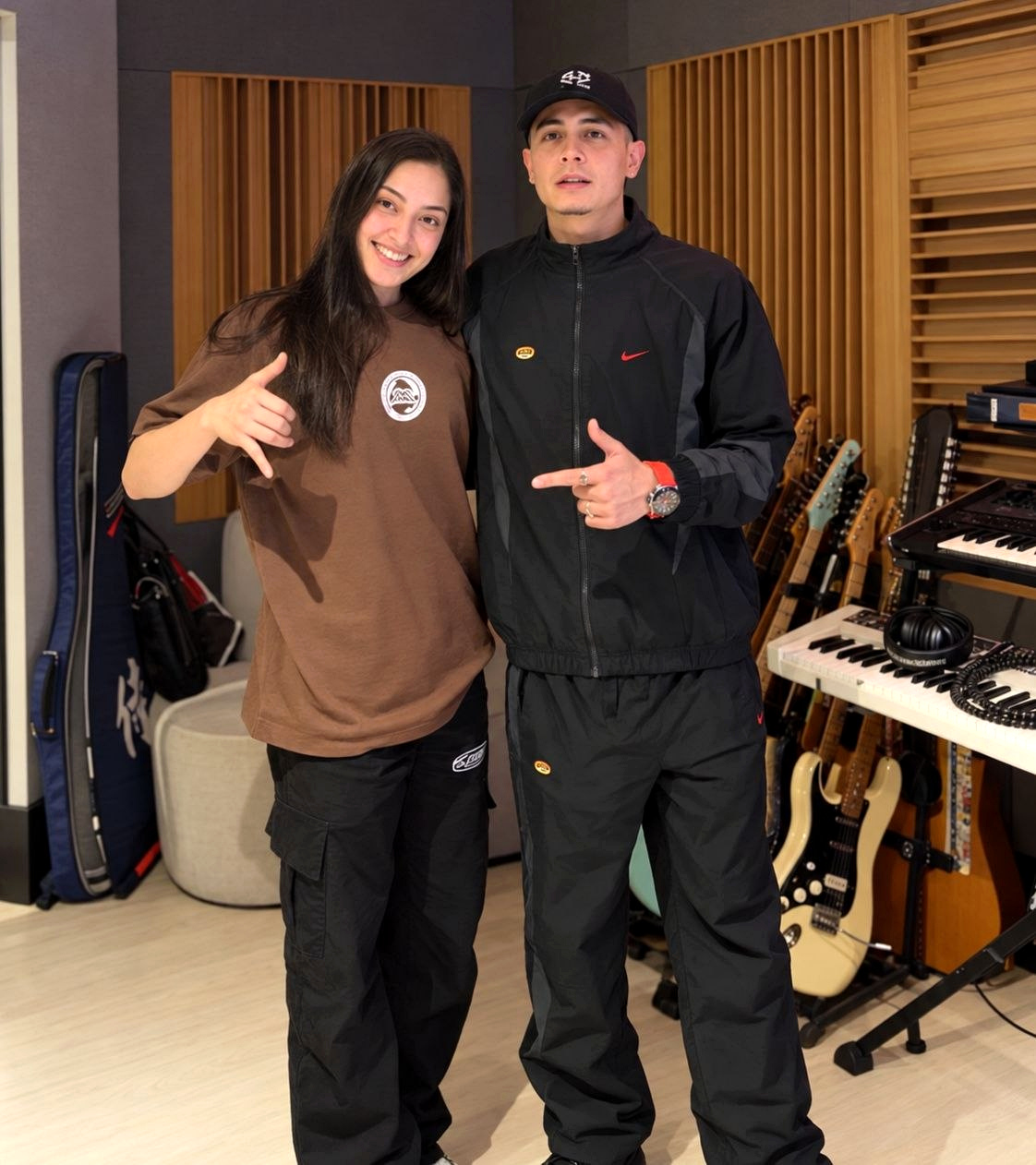 MC Coutto e Hariel posam lado a lado em estúdio, com guitarras e teclados ao fundo