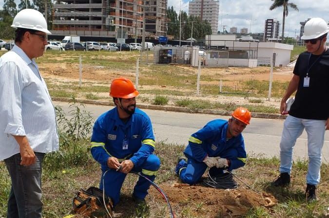 Trabalhadores manuseiam cabos em uma caixa de passagem aberta junto à via, perto do Boulevard Shopping.