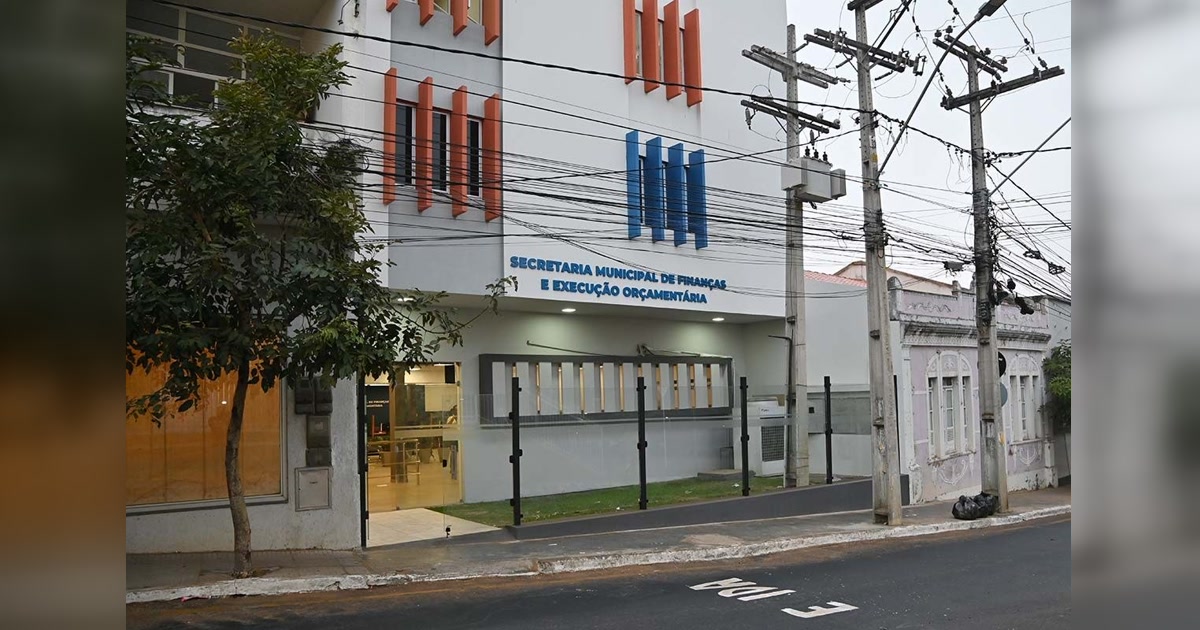 Fachada da Secretaria Municipal de Finanças e Execução Orçamentária, com entrada de vidro e rede elétrica à frente